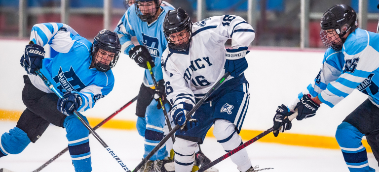 Quincy college ice hockey player surround by three opponent team players