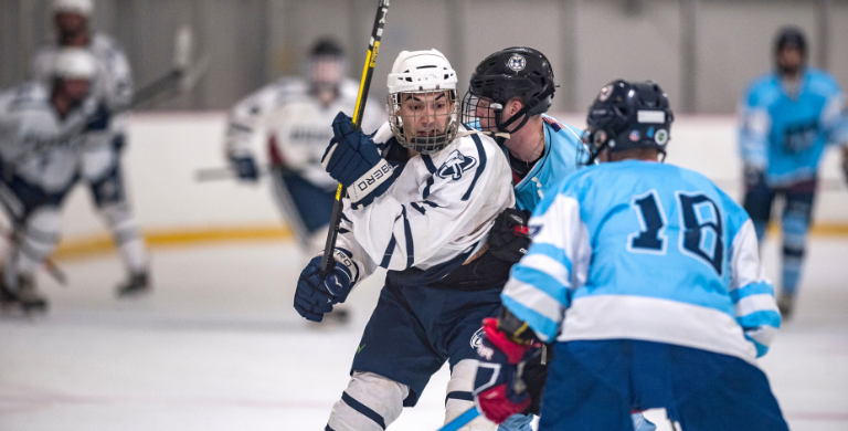 Quincy college ice hockey player surround by opponent team players